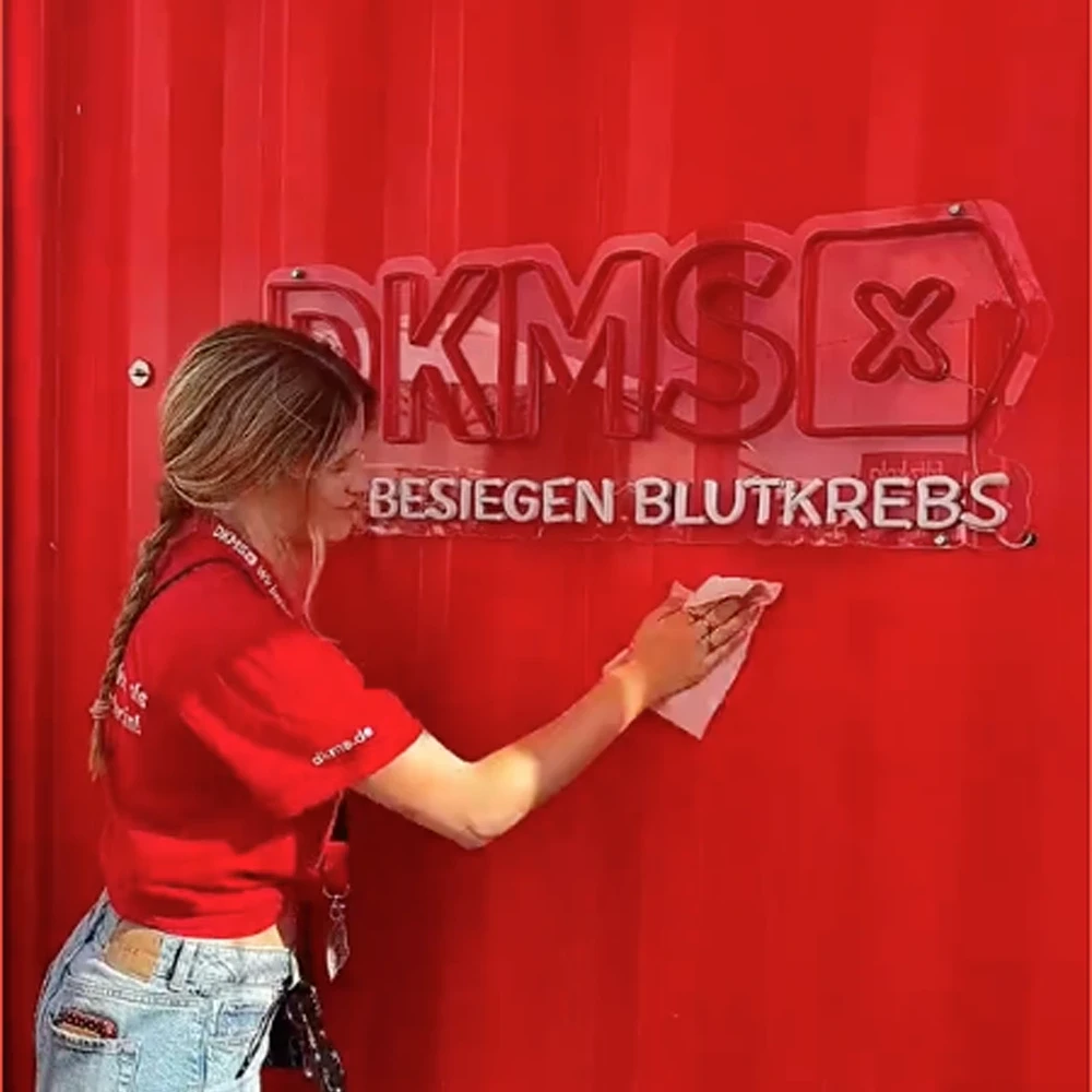 Eine junge Mitarbeiterin am DKMS-Festivalstand reinigt einen roten Container mit DKMS-Schriftzug.