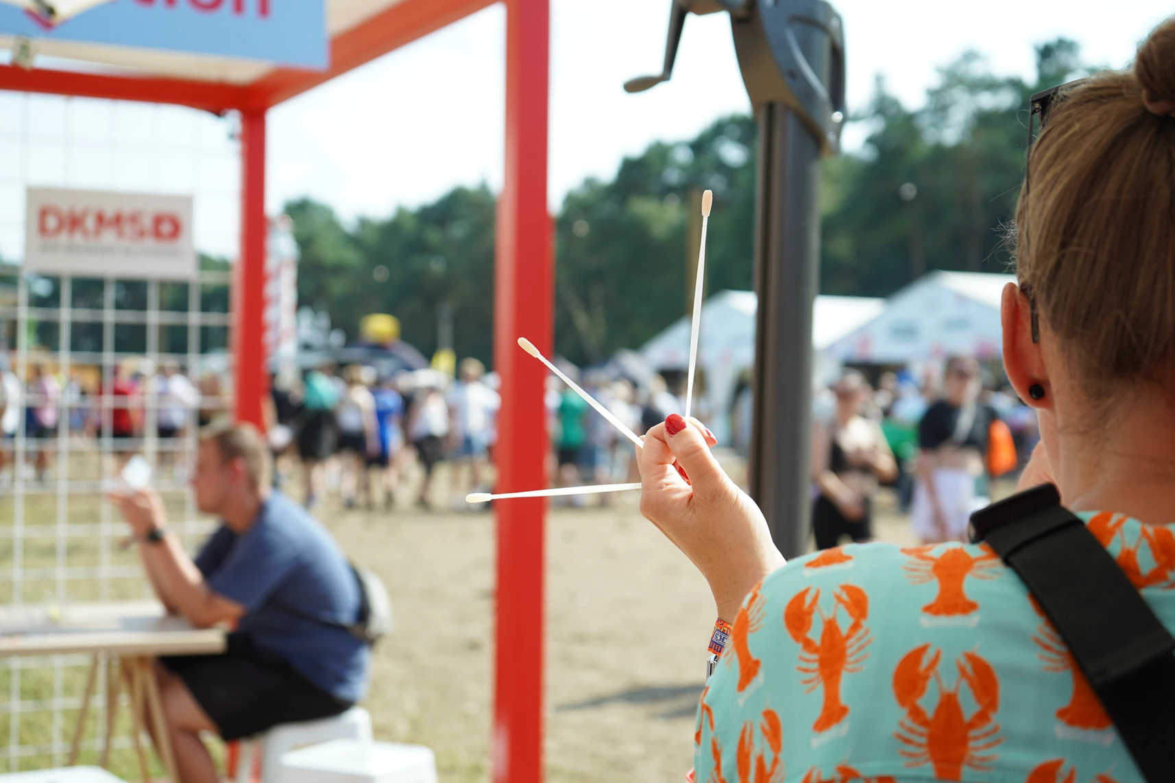 Eine Mitarbeiterin am DKMS-Festivalstand hält Wattestäbchen für die Typisierung in der Hand.