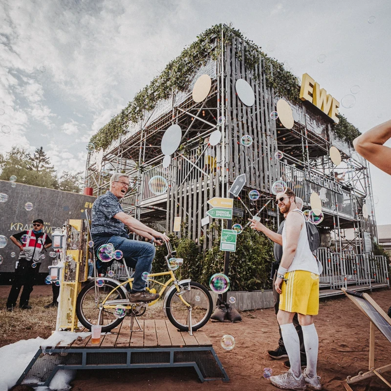 Ein Festivalbesucher erzeugt auf dem EWE Kraftwerk spielerisch mit einem Fahrrad &Ouml;kostrom, w&auml;hrend andere Besucher die interaktive Installation erleben.