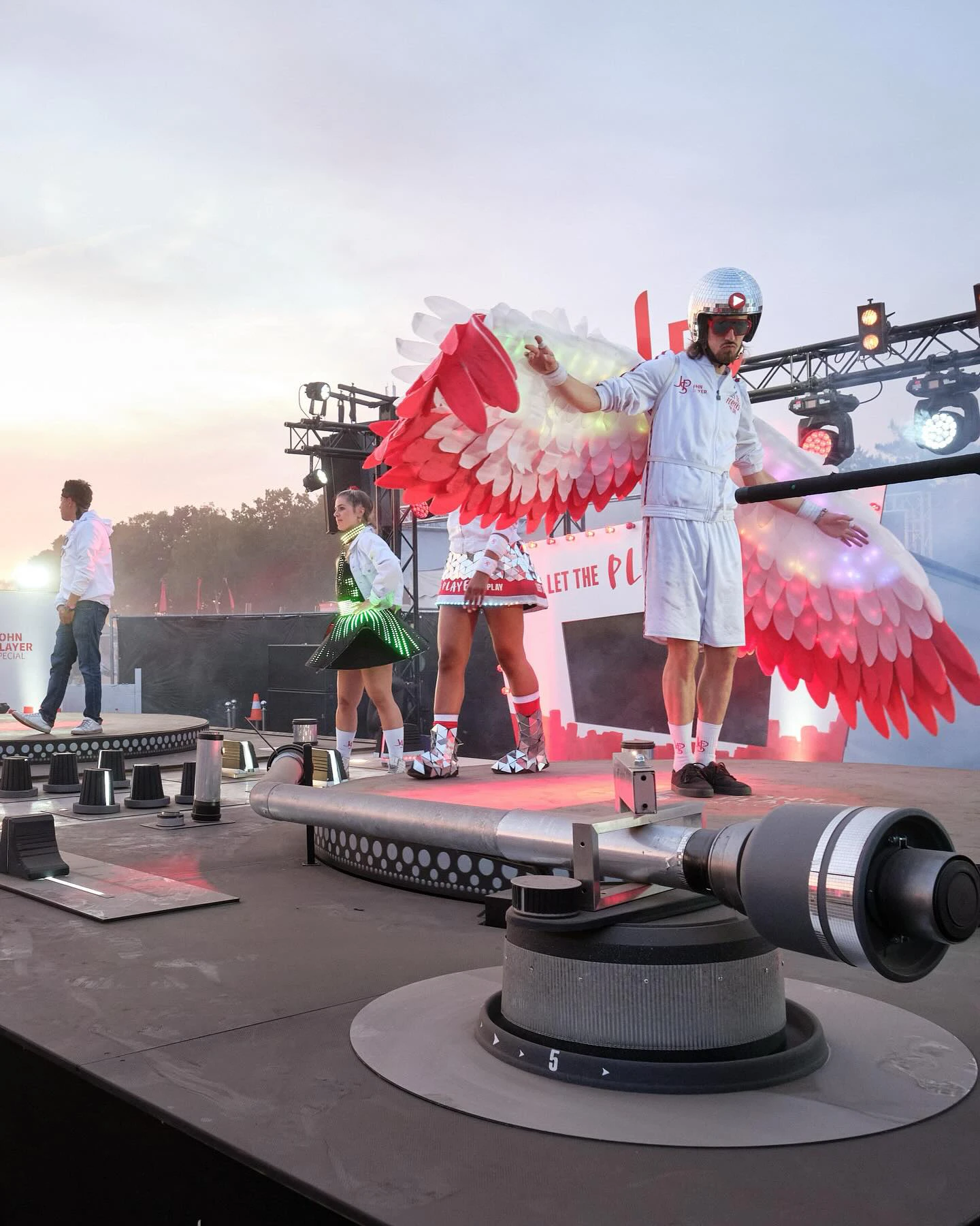Ein Promoter der JSP-Festival-Tour steht mit leuchtenden Flügeln auf einem begehbaren XXL-Plattenspieler.