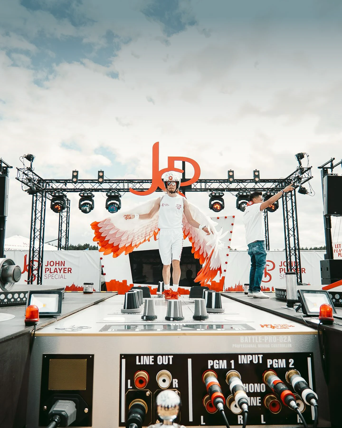 Ein Promoter mit auff&auml;lligem Fl&uuml;gelkost&uuml;m auf einem begehbaren XXL-Festival-Plattenspieler.