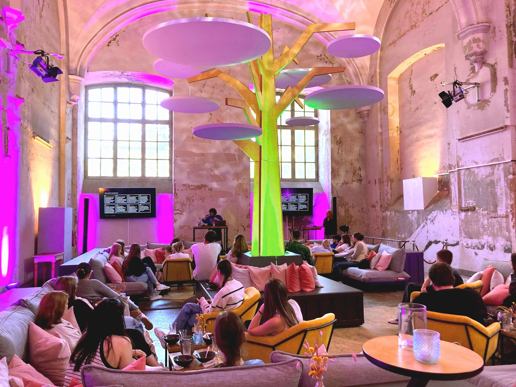 Besucher sitzen unter der illuminierten Bauminstallation während einer Veranstaltung in der „Umgedrehten Kommode“ in Bremen.